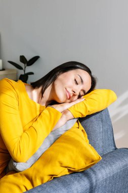 Evdeki kanepede dinlenen genç ve güzel bir kadın. Modern apartmandaki kanepede uyurken açık havada güneş ışığının tadını çıkaran oldukça modern bir kadın. Refah kavramı. Dikey fotoğraf.