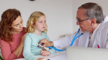 Pediyatrist kıdemli doktor muayene odasında küçük bir kızın kalp atışlarını ve nefes alışlarını dinliyor. Çocuk sağlığı konsepti.