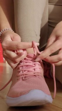 Vertical video. Close-up view of female hands tying laces of her sport shoes before home workout exercise routine. Motivation, healthy lifestyle and fitness concept.