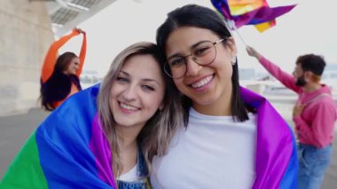 Gay Onur Günü 'nü kutlayan insanların kameraya gülümseyen genç lezbiyen çiftin yavaş çekim videosu. LGBTQ ve aşk konsepti