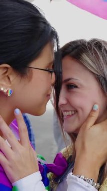Lezbiyen çift LGBTQ geçit töreninde öpüşüyor. Birbirini seven iki genç kız arkadaş LGBT onur gününü kutluyor. Dikey HD video.