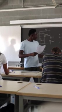 Genç Afrikalı lise öğrencisinin sunum yaptığı dikey HD video. Genç çocuk üniversite dersinde bir iş sunuyor. Sınıfa katılan bir grup öğrenci.. 