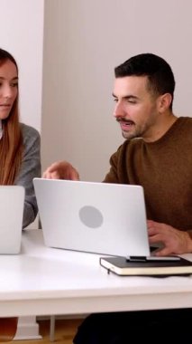 İş projesini tartışan iki genç iş adamı ofiste dizüstü bilgisayarda birlikte çalışıyorlar. Dikey HD video