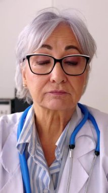 Hastanedeki tıbbi konsültasyondan gelen dizüstü bilgisayarla hastayla konuşan yaşlı kadın doktorunun dikey görüntüsü. Klinik yardım ve teletıp kavramı. 