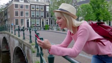 Amsterdam 'da akıllı telefon kullanan mutlu genç bir turist. Teknoloji ve seyahat yaşam tarzı konsepti.