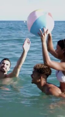 Dikey video. Genç bir arkadaş grubu yaz tatilinde plaj topuyla oynarken eğleniyor.