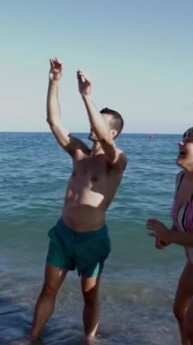 Dikey video. Genç bir arkadaş grubu yaz tatilinde plaj topuyla oynarken eğleniyor. Yaz dönemi yaşam tarzı kavramı.