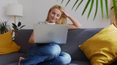 Evdeki rahat koltukta dizüstü bilgisayar kullanan mutlu genç kız. Eğitim yaşam tarzı ve teknoloji kavramı.