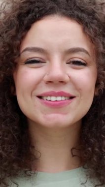Dışarıda kameraya bakan mutlu genç bir kadının yakın plan yüz portresi. Dişli gülüşü olan pozitif insanlar. Dikey video.