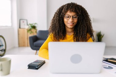 Evde dizüstü bilgisayarda çalışan Afro-Amerikalı genç bir kadın. Eğitim ve iş konsepti.
