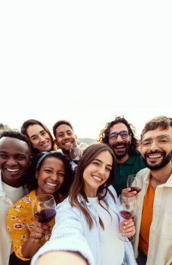 Mutlu genç arkadaşların selfie grubunu alıp yaz partisinin tadını çıkardıkları dikey bir çekim. Milenyum insanları çatıdaki kutlamalarda kırmızı şarap içerek eğleniyor. Metin için alanı kopyala.