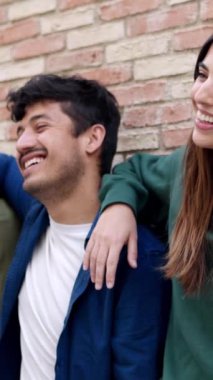 Dikey video. Açık havada birlikte gülen mutlu genç arkadaşlar. Çok ırklı insanlar birbirlerine sarılıp eğleniyorlardı. Gençlik toplumu ve halk kavramı.