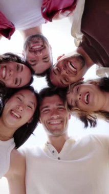 Dikey video. Kameraya gülümseyen mutlu bir grup gencin düşük açılı görüntüsü. Çeşitli arkadaşlar dışarıda birlikte eğleniyorlar. Arkadaşlık, çeşitlilik ve toplum konsepti.