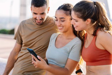 Egzersiz sonrası cep telefonu kullanan üç genç sportif arkadaş. Teknoloji yaşam tarzı ve uygunluk kavramı