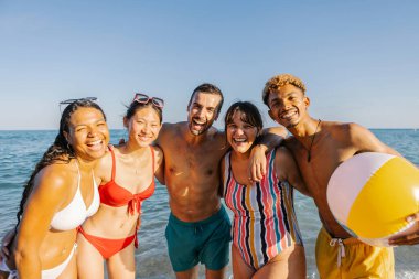 Yaz tatili boyunca sahilde birbirine sarılan farklı arkadaşların portresi.