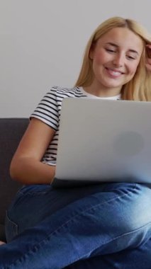 Evdeki rahat koltukta dizüstü bilgisayar kullanan mutlu genç kız. Eğitim yaşam tarzı ve teknoloji kavramı. Dikey 9: 16 videosu.