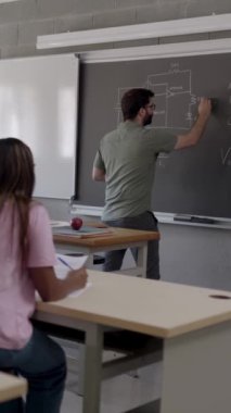 Teknoloji öğretmeninin dikey HD videosu. Çok ırklı lise öğrencilerine elektrik devresi dersi veriyor. Eğitim kavramı.