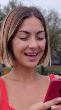 Yazın şehir caddesinde akıllı telefon kullanan mutlu sarışın bir kadının dikey HD videosu. Teknoloji ve gen teknolojisi kavramı.