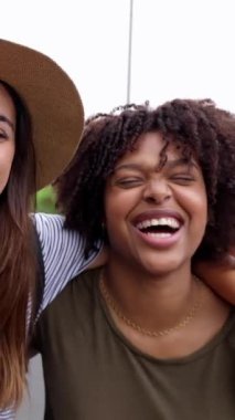 Dışarıda kameraya gülümseyen üç mutlu çok ırklı genç kadının dikey videosu. Birleşmiş Milenyum kadın arkadaşlarının neşeli portresi. Eğleniyorlar, hafta sonu kaçamağının tadını çıkarıyorlar.. 