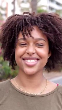 Açık havada kameraya gülümseyen kıvırcık saçlı neşeli Afrikalı Amerikalı kadının dikey HD videosu..