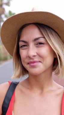 Dışarıda kameraya gülümseyen şapkalı güzel sarışın kızın dikey portresi. Mutlu İspanyol bayan turist yaz gününün tadını çıkarıyor..