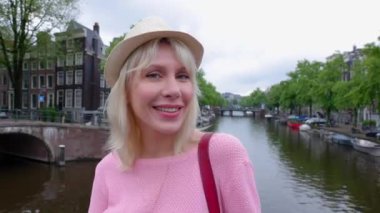 Amsterdam caddesinde kameraya gülümseyen Hollandalı genç kadının çekici portresi. Hollanda 'da yaz şapkalı neşeli çekici bayan turist. Seyahat yaşam tarzı konsepti.