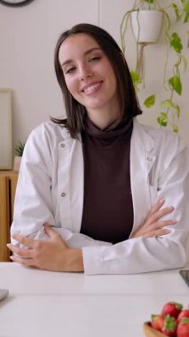 Dikey HD video. Tıbbi muayenede kameraya gülümseyen genç ve güzel beslenme uzmanı kadının portresi. Profesyonel sağlık çalışanı konsepti