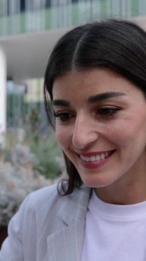 Uzaktan kumandayla çalışan mutlu genç bir kadın ofis merkezinin dışında oturuyor. Girişimciler ve iş konsepti. Dikey HD video. 