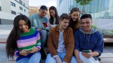 Açık havada akıllı telefon kullanan mutlu bir grup genç arkadaş. Milenyum kuşağı insanları sosyal medya uygulamasında içeriği paylaşırken eğleniyor. Teknoloji, arkadaşlık ve gençlik kavramı