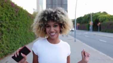 City Street 'te dans eden mutlu Latin Amerikalı kadın. Bin yıllık etnik bir kızın telefonda dans müziğinin keyfini çıkarırken kameraya gülümseyişinin yavaş çekim görüntüsü. Tasasız ve mutluluk konsepti