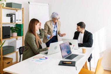 Bilgisayarlı iş adamları ofiste yeni proje fikirlerini tartışıyor.