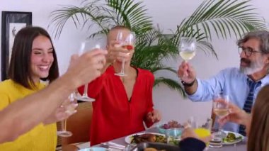 Mutlu bir aile grubu evde öğle yemeğinin tadını çıkarırken kadeh kaldırıyor.