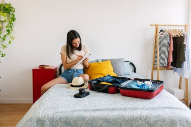 Genç ve güzel bir kadın listeyi yapıyor, tatilden önce yaz valizini hazırlıyor. Yaz yaşam tarzı konsepti.