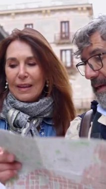 Barselona 'da yürüyüş yaparken elinde şehir haritası tutan mutlu yaşlı turist çifti. Evli, orta yaşlı bir adam ve kadın seyahat sırasında telefon uygulamasında turistik bir yer arıyorlar. Dikey video