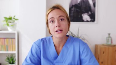 Genç sağlık çalışanlarının POV 'u evden bir video görüşmesi yapıyor. Mavi önlüklü gülümseyen genç bayan hemşire hastayla sanal konferans aracılığıyla konuşuyor. Teletıp kavramı.