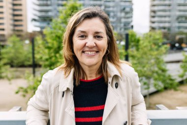 Şehrin arka planında kameraya gülümseyen mutlu son sınıf kadını. Şehir caddesinde 60 'ların kadın portresi.