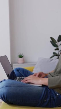 Evdeki rahat koltukta dizüstü bilgisayar kullanan mutlu genç kızın dikey HD videosu. Eğitim yaşam tarzı ve teknoloji kavramı.