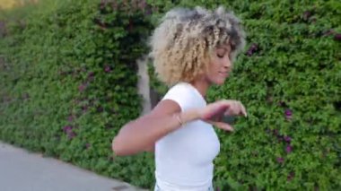 Heyecanlı, Afro-Amerikan bir kadının şehir caddesinde dans ederken telefonla müzik dinlemesinin yan görüntüsü. Tasasız, kutlama ve mutluluk konsepti