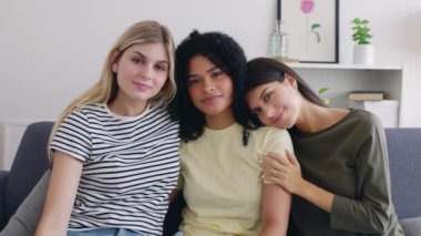 Kanepede birlikte oturan üç farklı yetişkin bayan arkadaşın portresi. Çok ırklı kızlar kameraya bakıyor birbirlerine sarılıyorlar kanepede dinleniyorlar. Kadın arkadaşlığı kavramı.