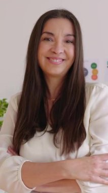 Yetişkin bir iş kadınının ofiste kameraya bakarken çekilmiş dikey HD videosu. Profesyonel kadın yöneticinin gülümsemesi ön planda. İş adamları konsepti.