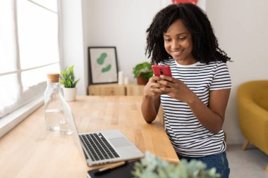 Mutlu Milenyum Afro-Amerikan kadın akıllı telefondan mesajlaşıyor. Neşeli Brezilyalı kadın dizüstü bilgisayarla çalışırken telefonda sosyal medya içeriğini izliyor