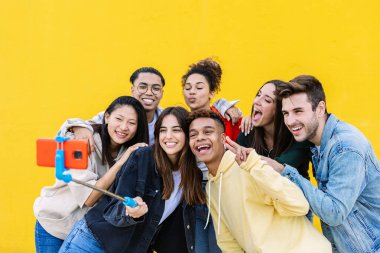 Mutlu genç arkadaşlar fotoğraf çekiyor. Akıllı telefon ve selfie çubuğu kullanıyor.
