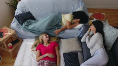 Pijama partisinde yattıktan sonra eğlenen üç mutlu genç bayan arkadaş. Milenyum çeşitliliği olan kadın gülüyor, evdeki yatakta dinleniyor..