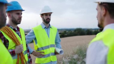 Bir grup teknisyen ve mühendis rüzgar türbinleri çiftliğinde konuşuyorlar - yenilenebilir ve alternatif enerji kavramı