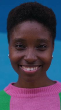 Dikey HD video. Açık havada kameraya gülümseyen gülümseyen genç siyahi kadının portresini yakından çek..