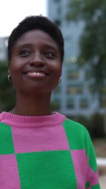 Gülümseyen trend genç siyahi kadının şehir caddesinde yürüdüğü dikey HD video