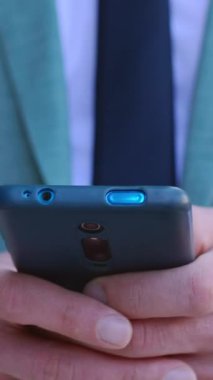 Açık havada akıllı telefon aygıtı kullanan işadamlarının dikey HD videosu. Takım elbiseli profesyonel erkek, dokunmatik cihaz ekranında cep telefonuyla mesaj yazıyor..
