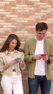 Genç bir adam ve kadın şehir duvarının üzerinden cep telefonu kullanıyor. Teknoloji konsepti. Dikey video.