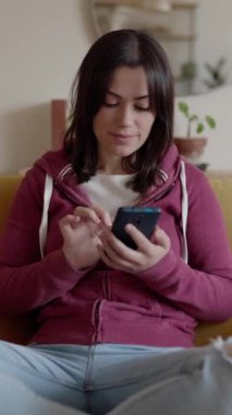 Beklenmedik bir mesajla kötü haber okuyan genç bir kadının dikey HD videosu ya da evdeki koltukta dinlenirken cep telefonunda e-posta.. 