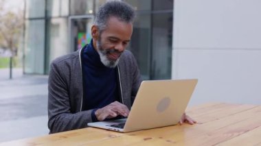 Üst düzey Afro-Amerikan iş adamı laptopta çalışıyor açık masada oturuyor. Başarılı bir yetişkin profesyonel işçi e-postaları kontrol ediyor ya da dışarıda internette sörf yapıyor..